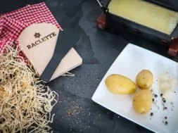 Queijo raclette sendo aquecido com batatas, cebolas e picles ao lado