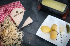 Queijo raclette sendo aquecido com batatas, cebolas e picles ao lado