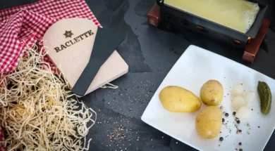 Queijo raclette sendo aquecido com batatas, cebolas e picles ao lado