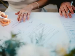 Imagem de um casal assinando documentos no casamento civil, em uma mesa simples, com caneta em mãos e clima formal.