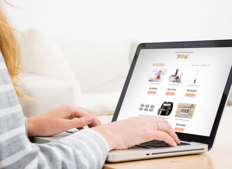 Pessoa navegando em notebook por uma lista online de presentes de casamento, com itens domésticos e valores exibidos na tela.