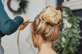 Imagem mostra uma mulher em um salão de beleza, fazendo um penteado com a ajuda de um profissional, que trabalha cuidadosamente em seu cabelo