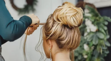 Imagem mostra uma mulher em um salão de beleza, fazendo um penteado com a ajuda de um profissional, que trabalha cuidadosamente em seu cabelo
