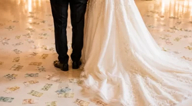 Noivos vistos de costas em festa de casamento, com notas de dinheiro espalhadas pelo chão ao redor do vestido da noiva.