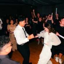 Noivos dançando animados no centro da pista enquanto convidados comemoram ao redor, ilustrando a escolha de músicas para casamento animar a festa.