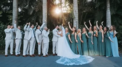 Imagem de um casal de noivos no centro, cercado por vários padrinhos e madrinhas, com árvores ao fundo.