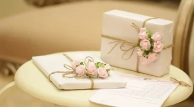 Imagem de dois presentes brancos decorados com flores rosas e barbante sobre uma mesa, com um envelope de carta.
