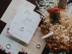 Imagem de convites de casamento com um anel sobre eles e, ao lado, flores decorativas