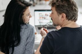 Casal juntos em mesa com notebook fazendo site de casamento.
