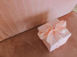 Caixa de presente decorada com laço rosa sobre um sofá, representando uma opção simples e elegante de presente de última hora de casamento.