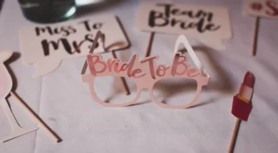 Óculos decorativos de despedida de solteira com a frase “Bride to Be”, cercados por plaquinhas temáticas e um acessório em formato de batom.