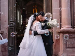 Noivos se abraçam na saída da cerimônia de casamento, cercados por bolhas de sabão.