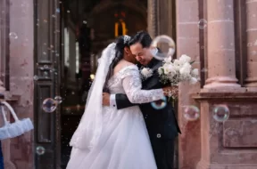 Noivos se abraçam na saída da cerimônia de casamento, cercados por bolhas de sabão.