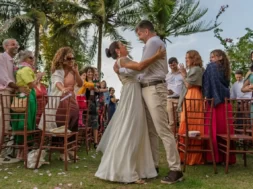 Noivos se abraçam durante cerimônia de casamento ao ar livre, cercados por convidados em um jardim.