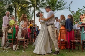 Noivos se abraçam durante cerimônia de casamento ao ar livre, cercados por convidados em um jardim.